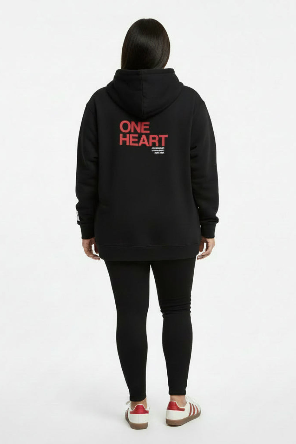 Woman wearing a black hoodie with 'ONE HEART' text on the back against a white background