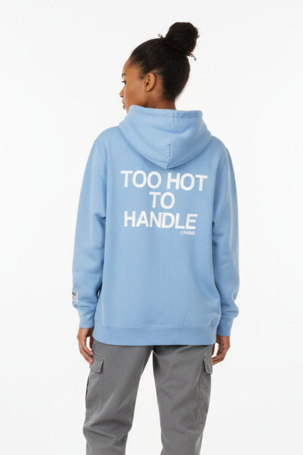Woman wearing a light blue hoodie with 'Too Hot To Handle' text on the back, standing against a white background.