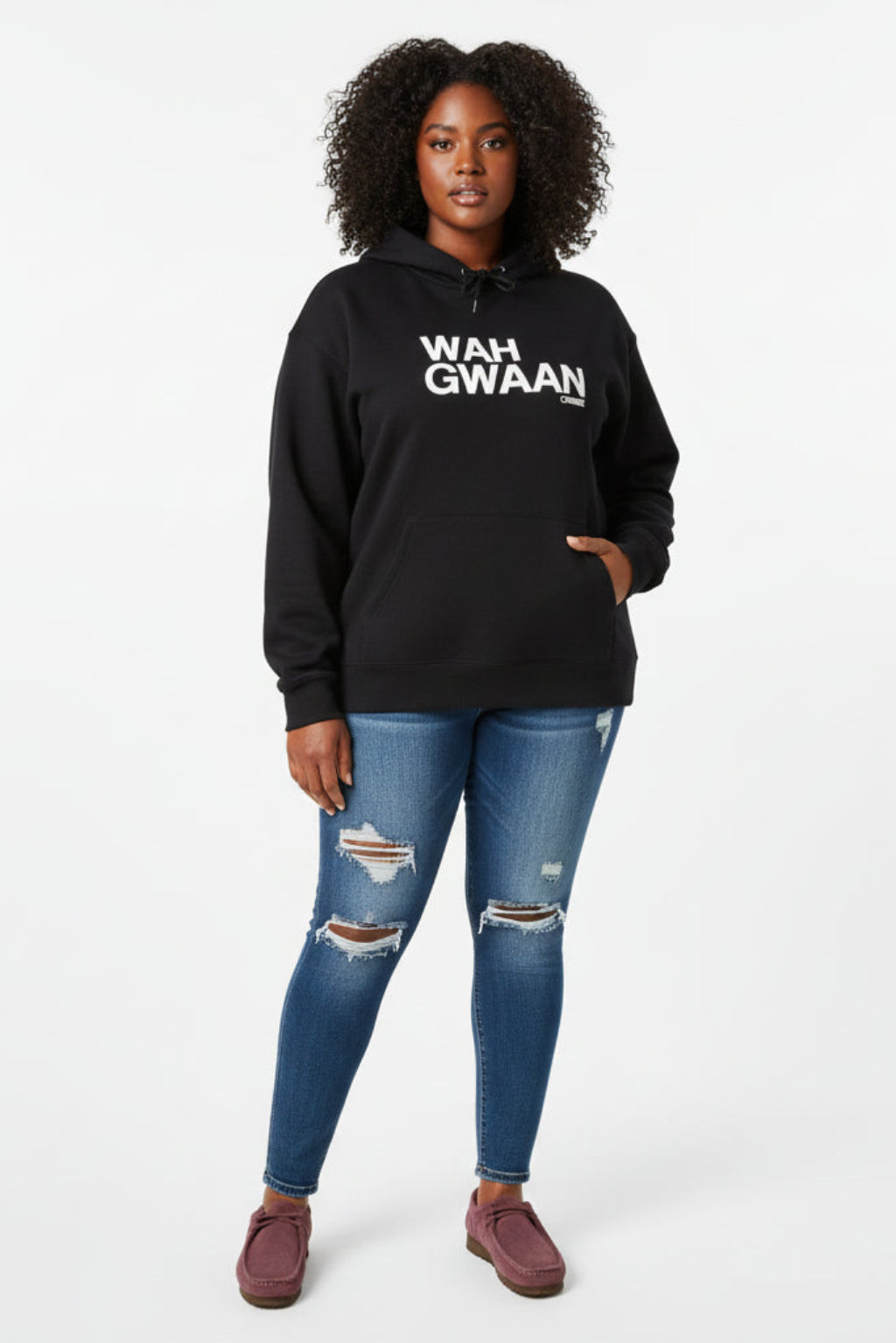 Women wearing a black hoodie with 'WAH GWAAN' text, ripped jeans and a pair of Clarks Wallabees  on a white background